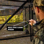 Man cleaning window with tool, showcasing TIDEWE hunting blind's see-through material and camo design. Product: Hunting Blind See Through with Carrying Bag, Pop Up Ground Blinds 270 Degree.