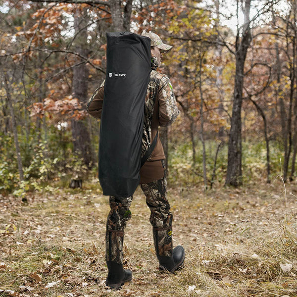 Man in camouflage holding a black bag in woods, showcasing TIDEWE Hunting Blind See Through with Carrying Bag, Pop Up Ground Blinds 270 Degree.