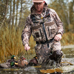 Man in camouflage gear using DeepWade Zipped Duck Waterfowl Hunting Breathable Chest Waders, standing in a river, holding a rope with ducks nearby.