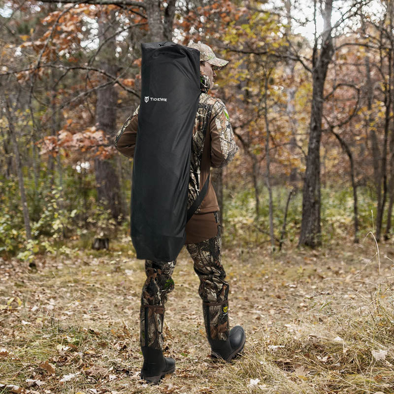 Man in camouflage carrying a black bag stands in the woods, showcasing the Occult See Through Hunting Blind 2-3 Person Pop Up Ground Deer Blind.