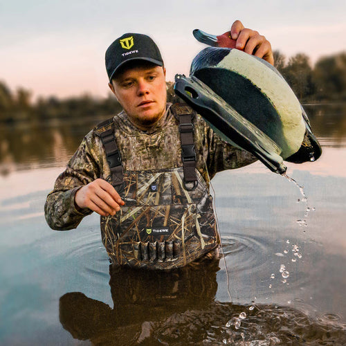 Man wearing TorridSeeker Heated Duck Waterfowl Hunting Neoprene Chest Waders, standing in water, pouring into a bucket, showcasing rugged durability and smart heating features.